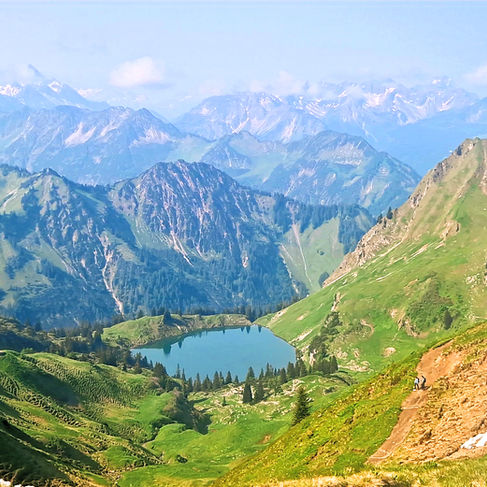 Summer view of the Oberstdorf mountains with a turquoise alpine lake in a green valley and rugged peaks all around.