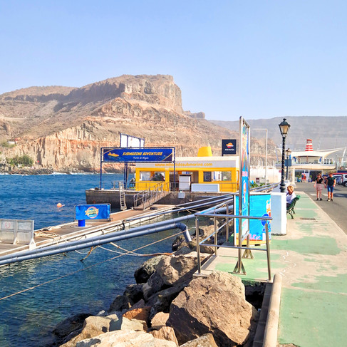 Pier and Yellow Submarine station in Puerto Rico, Gran Canaria, with boats, cliffs, and marina walkway.