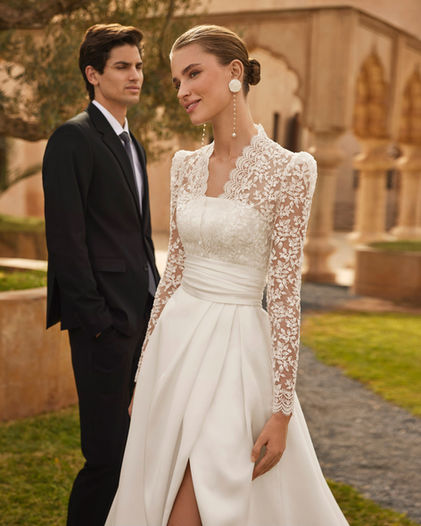 Robe de mariée Orbe de Rosa Clará, une coupe moderne, bustier en mikado, satin ou tissu Sienne, disponible avec ceinture, boléro en dentelle et col amovibles, en vente chez Noces de Cristal à Nancy.