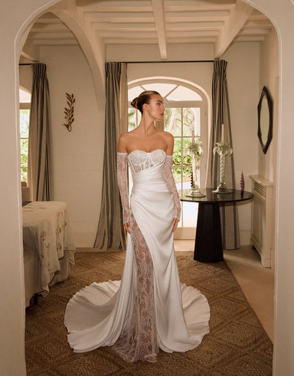 Robe de mariée Eugénie d’Alberto Palatchi, coupe sirène moderne alliant buste en dentelle délicate à une jupe drapée en satin, avec une fente latérale, manches longues amovibles et jupe en dentelle détachable pour deux styles en un. Disponible chez Noces de Cristal à Nancy