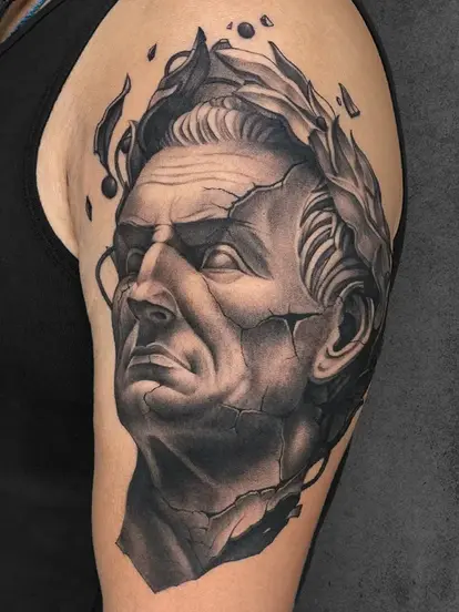 A shoulder tattoo styled like an ancient Roman statue with cracks and subtle decay, symbolizing strength and impermanence
