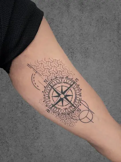 A fine line tattoo of a compass with geometric elements and a tire tread pattern, symbolizing exploration and travel, placed on the inner forearm