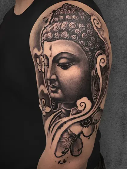 Buddha upper arm tattoo with butterflies and floral details, unisex, black and grey realism by Aliens Tattoo
