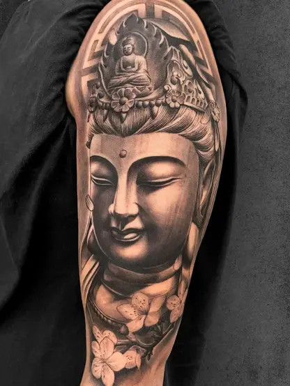 Buddha tattoo on upper arm, black and grey realism featuring intricate crown details and lotus flowers