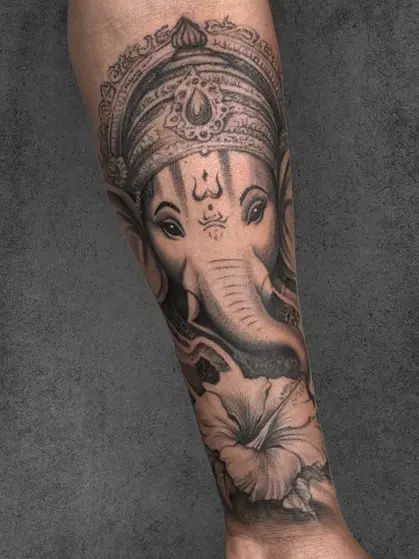 Ganesha forearm tattoo with floral detail, unisex, intricate black and grey realism by Aliens Tattoo