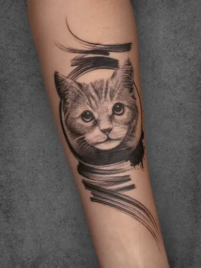 Cat portrait tattoo in black-and-grey realism with artistic brushstroke details, placed on the forearm.