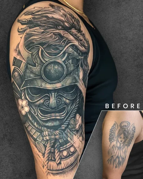 A detailed Japanese samurai mask tattoo on the upper arm, featuring intricate dragon elements. It beautifully conceals an older angelic figure tattoo seen in the inset