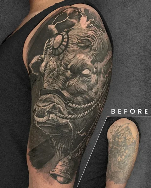 A highly detailed bull tattoo on the upper arm, featuring intense shading and dramatic elements. The design effectively conceals a heavily outlined tattoo visible in the inset.