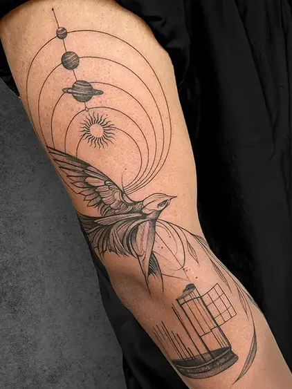 An artistic tattoo of a bird flying out of a cage with celestial symbols, representing freedom and exploration, designed by a student of the Complete Course in Tattoo
