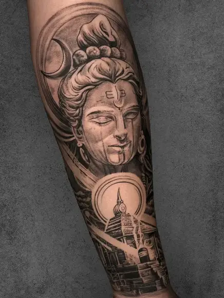 A tattoo depicting a serene Lord Shiva face with a crescent moon with temple and Shiva Linga below it, on a male's forearm, in realistic black and grey shading style
