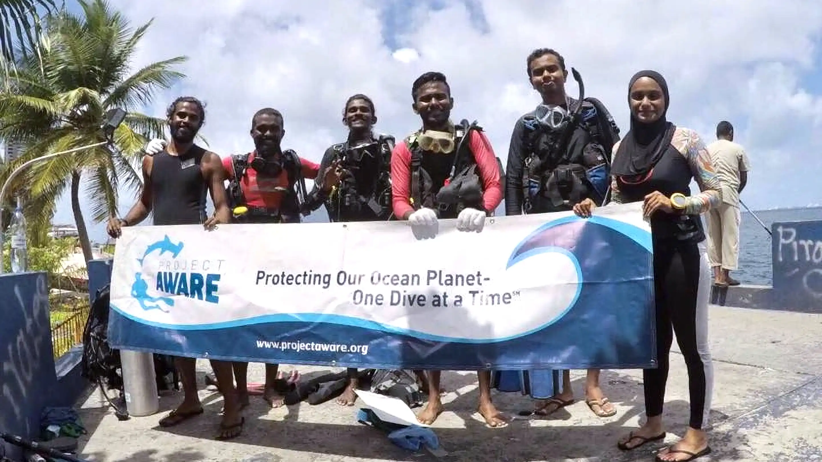 Project AWARE Specialist course participants holding the Project AWARE banner with Dive Desk Male' and the Maldivian Academy of Diving Himmafushi in the Maldives.