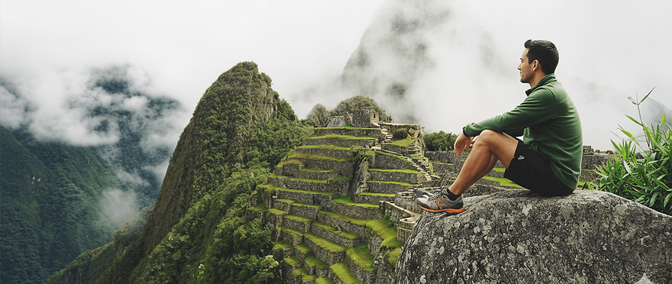 um homem sentado em uma pedra observando o vale sagrado de Machu Picchu