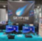 The booth layout at Ottawa Comic Con. The booth has a large banner with the SkyPyre Studios logo on it. In front of that are two computer monitors showing the main menu screen for the game called Mushroam.