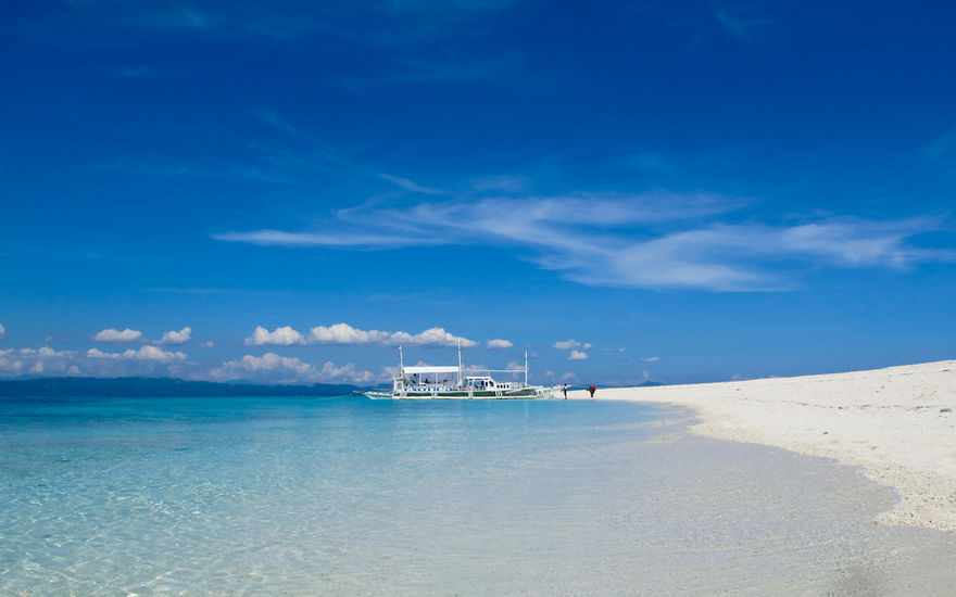 Bright blue sea with a boat near a white sandbar under clear skies