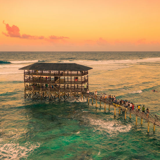 Overwater bungalow on stilts above shallow water during a warm orange sunset