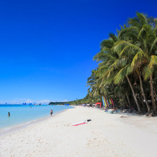 Wide stretch of Boracay white sand beach lined with palm trees under a bright blue sky
