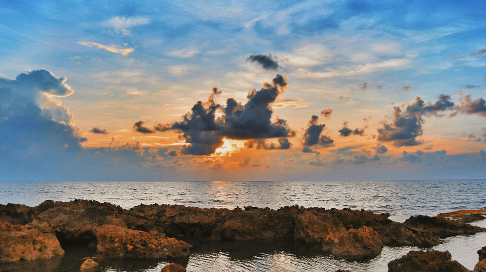 Rocky coastline at sunset with dramatic orange clouds over the ocean