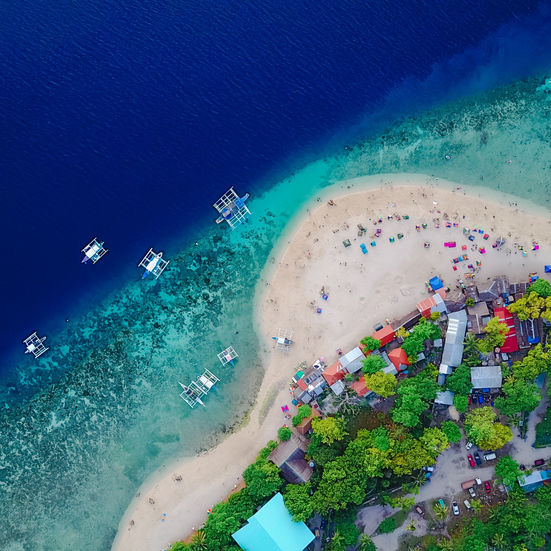 Small tropical sandbar island with colorful umbrellas and visitors surrounded by clear blue water