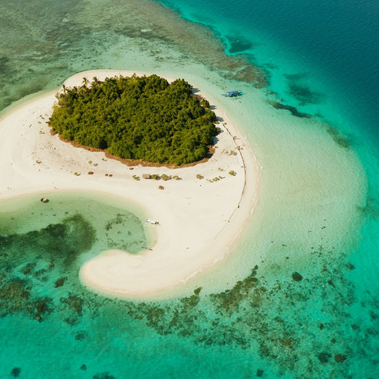 Small circular tropical island with lush greenery and shallow turquoise water
