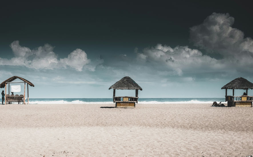 Sandy beach with a small hut or gazebo under a dark sky near the shoreline