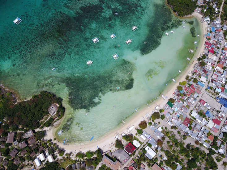 Aerial view of a coastal area with green water, shoreline buildings, and tropical vegetation