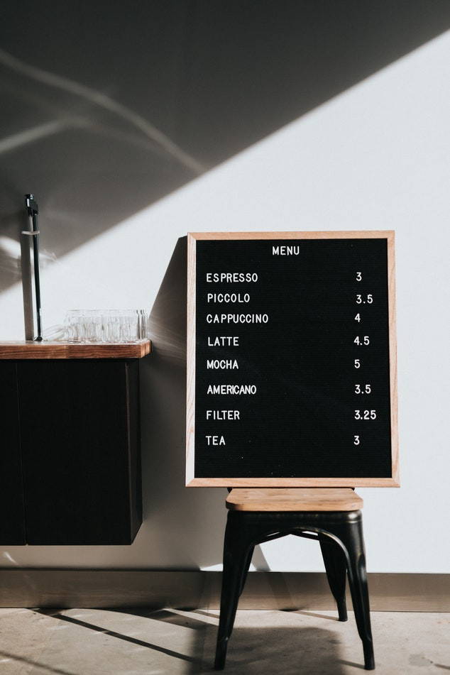 Menú de cafetería con opciones de café acompañado de sus precios en una pizarra estilo minimalista
