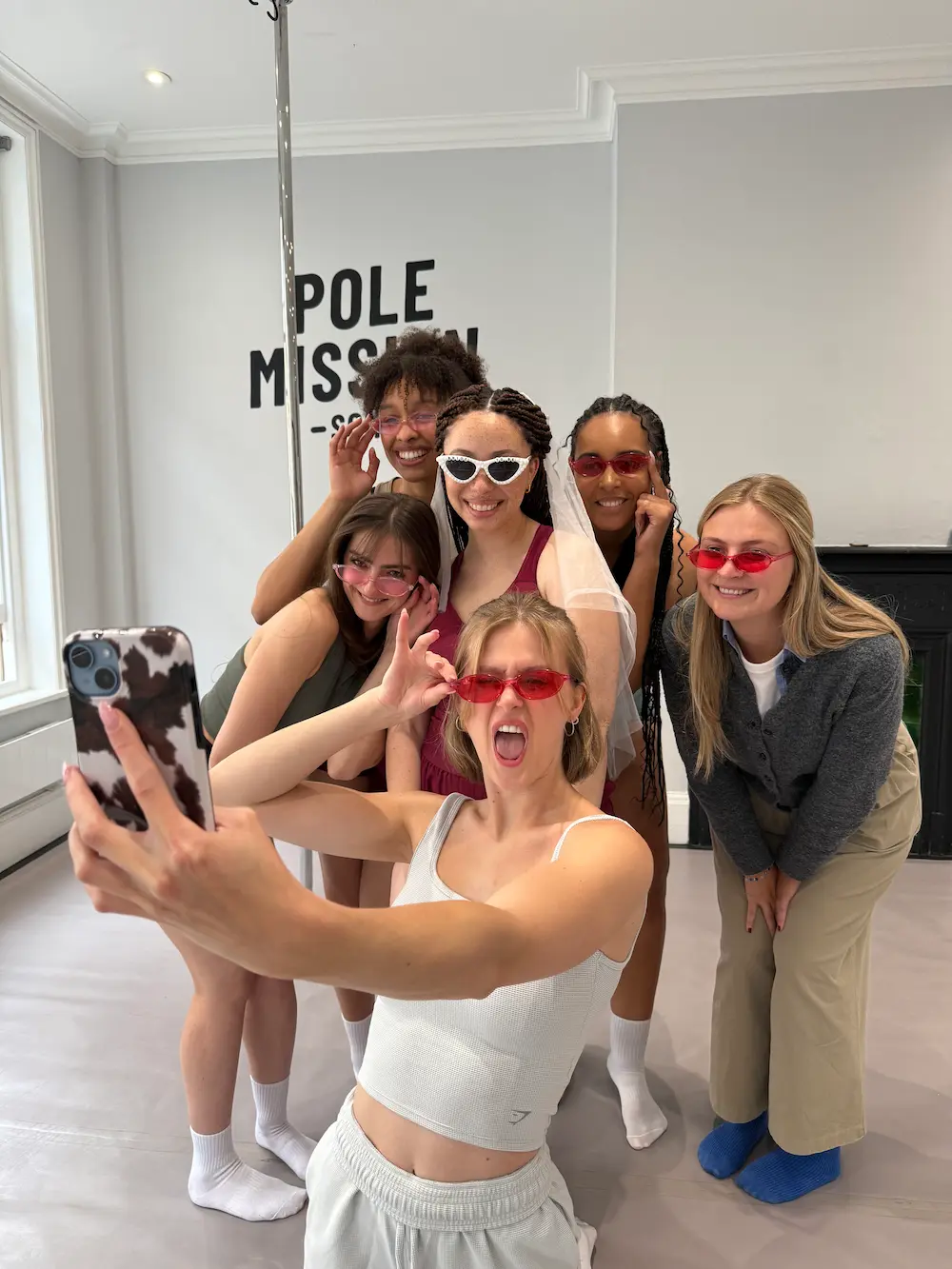 Hen-party group wearing sunglasses taking a mirror selfie inside Pole Mission’s central-London pole studio