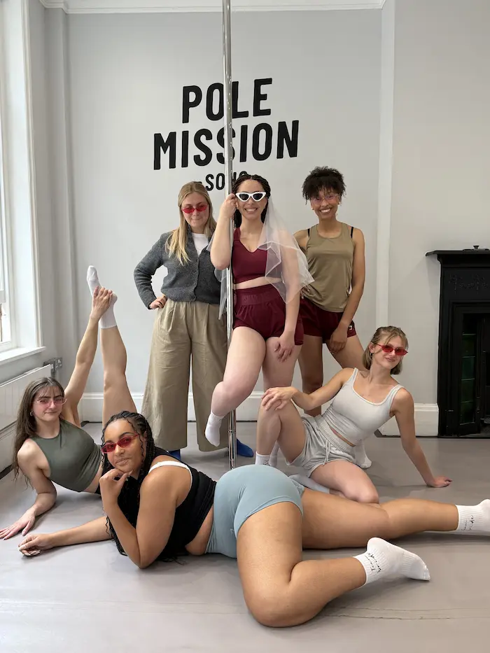 Friends sitting on the studio floor posing for a group shot after their pole-dance class in Soho hen weekend