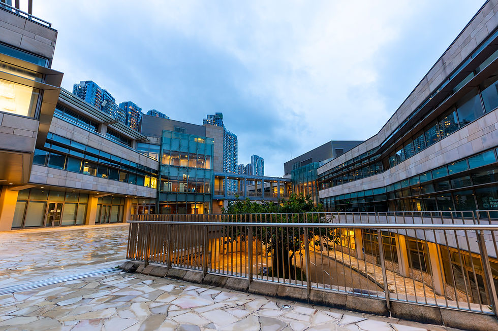 Modern urban buildings with glass facades at dusk, lit warmly from inside. Cloudy sky and high-rise apartments in the background.