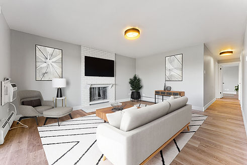 A spacious living room featuring a modern white sofa and a coffee table placed in the center, with a fireplace and a wall-mounted TV.
