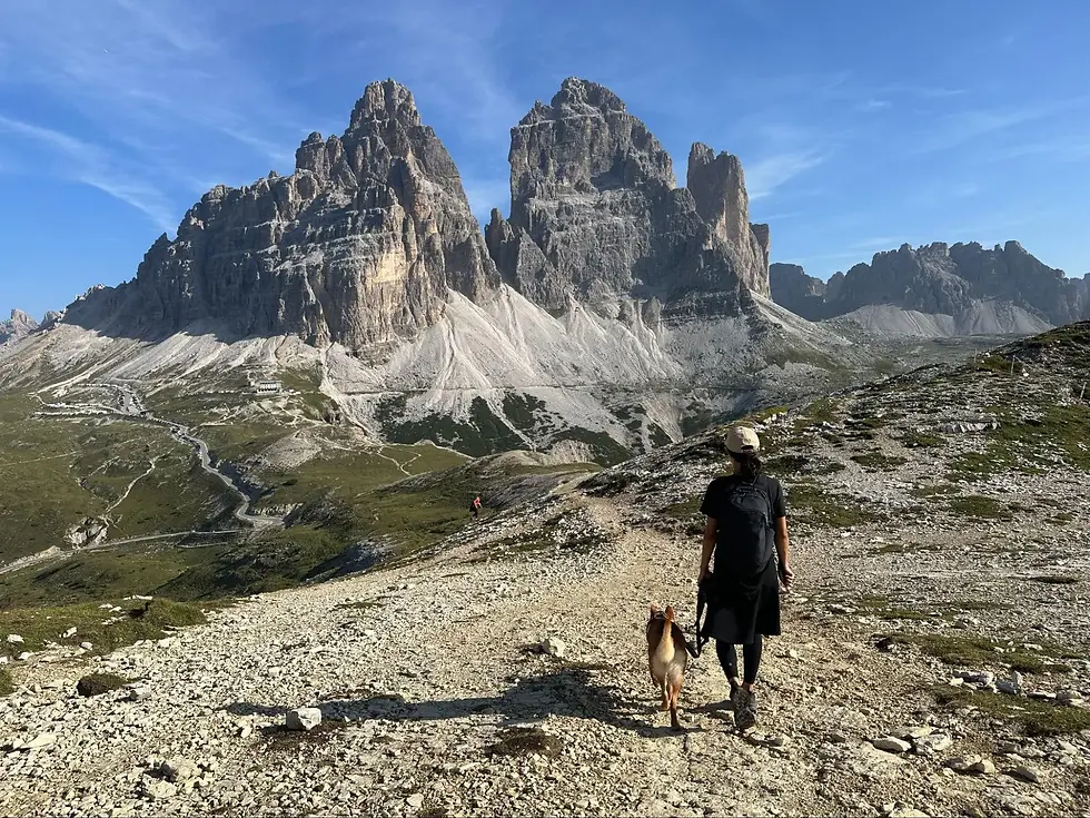 person walking with a dog on a mountain trail with a dramatic backdrop of rocky peaks