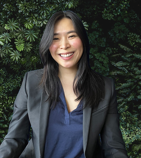 Alison in a black blazer smiling in front of a green background.