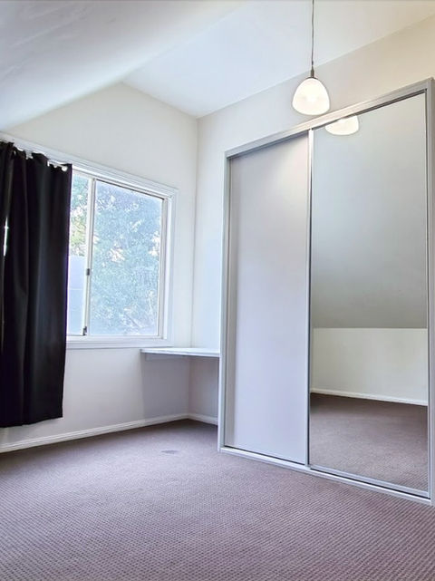 Sliding built-in wardrobe with mirror door and lid under raked ceiling