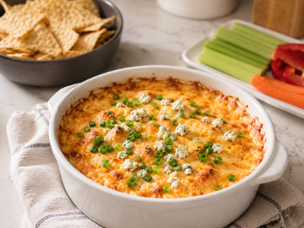 Hot Buffalo Chicken Dip baked until golden and bubbly, topped with green onions and blue cheese crumbles, served with tortilla chips, celery, and carrots.