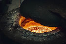 Glühendes, geschmolzenes Metall in einem industriellen Ofen mit dunklem Deckel.