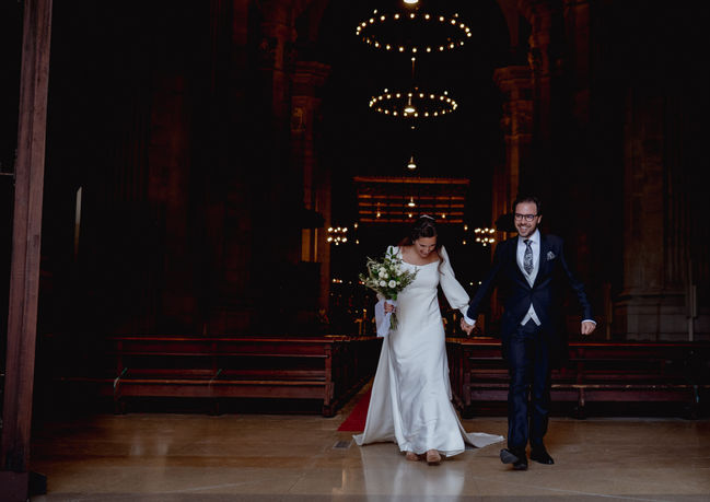 Salida de la Iglesia de los novios. Boda religiosa y novio con chaqué. Vestido de novia a medida en Barcelona. Vestido de escote corazón y corte en cintura alta decorado con tira bordada. Manga abullonada terminada en puño con botones y falda lisa evasé con vuelo en el bajo. Espalda abierta en forma cuadrada con pequeños pliegues hechos a mano y cierre en el centro con botones forrados pequeños. Desde la cintura, cola larga extraíble sujeta con botones forrados. Velo de mantilla. Vestido desmontable y versátil. Novia elegante. Novia diferente. Novia sencilla. Novia minimalista.
