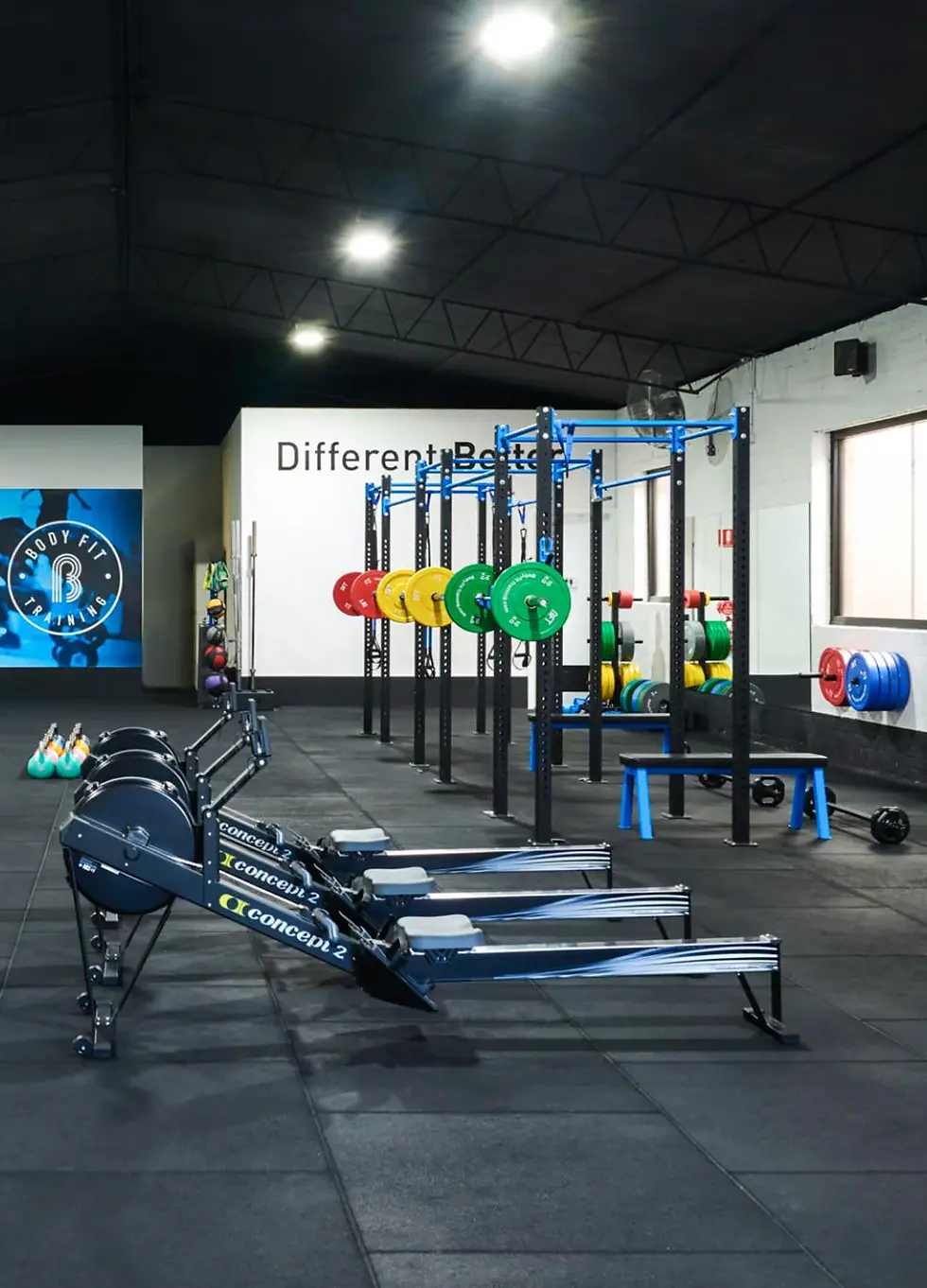 Interior of a modern fitness studio featuring rowing machines, squat racks, barbells, and strength training equipment.