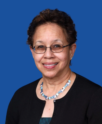 Smiling woman with glasses and a blue necklace against a solid blue background, wearing a black cardigan.
