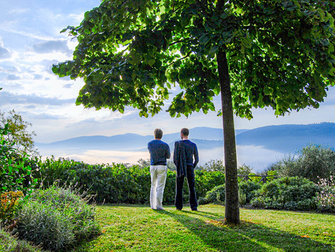 Spiritual teacher Daniel Hertlein looks out over a beautiful hilly landscape in Italy with a student. Both have their backs to the viewer.