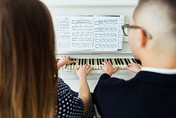 close-up-couple-playing-piano-with-musical-sheet.jpg