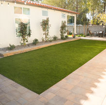 Green artificial turf backyard with beige patio and white house background