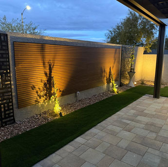 Modern backyard landscape at night with wood composite wall and lighting