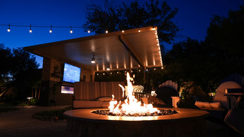 Outdoor living space with fire pit, patio cover, landscape lighting, and outdoor entertainment area at night