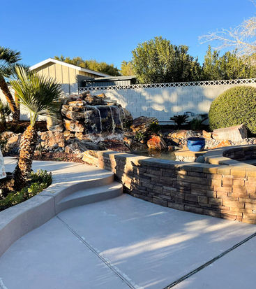 Backyard landscaping with rock waterfall, palm trees, and curved stone fire pit seating area.