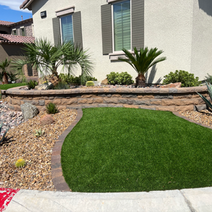 Landscaped yard with artificial turf and a stone wall.