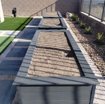 Modern raised garden beds made from composite decking in a minimalist backyard with gravel and pavers.