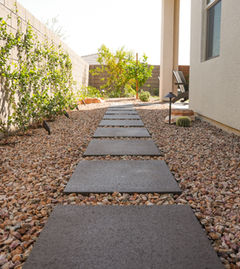 Stone walkway with gravel, wall, and a tree in the backyard