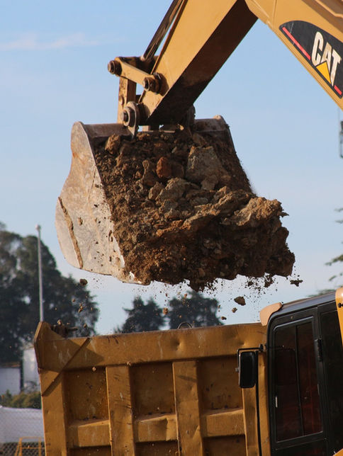 Yellow CAT Caterpillar excavator bucket dumping dirt into a truck
