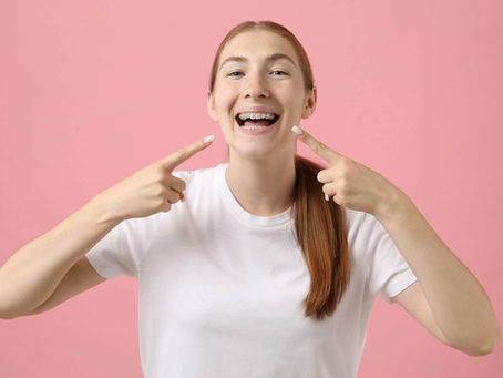 girl pointing her metal braces pink background - Clear Braces vs Metal Braces in Avon and Torrington, CT 