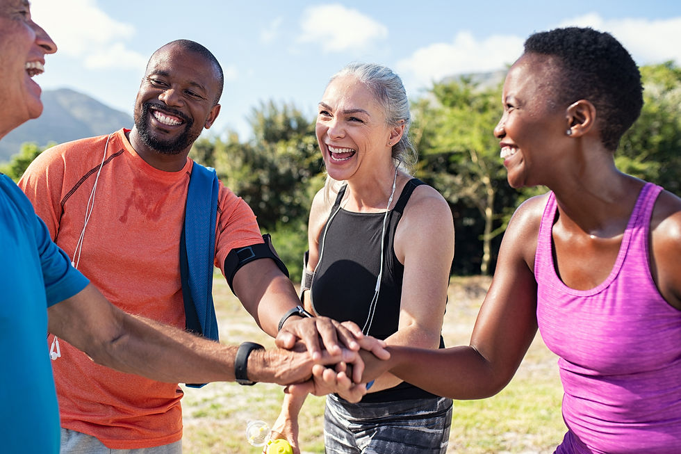 Four diverse individuals sharing a joyful moment outdoors, stacking hands and smiling after exercise.